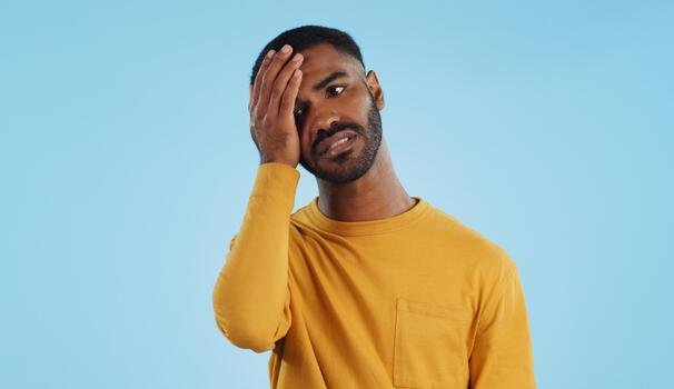 stress-fail-and-man-in-studio-with-facepalm-emoji-for-stupid-mistake-or-regret-on-blue-background-anxiety-oops-and-male-model-with-disaster-crisis-or-fake-news-shame-frustrated-and-unhappy-photo